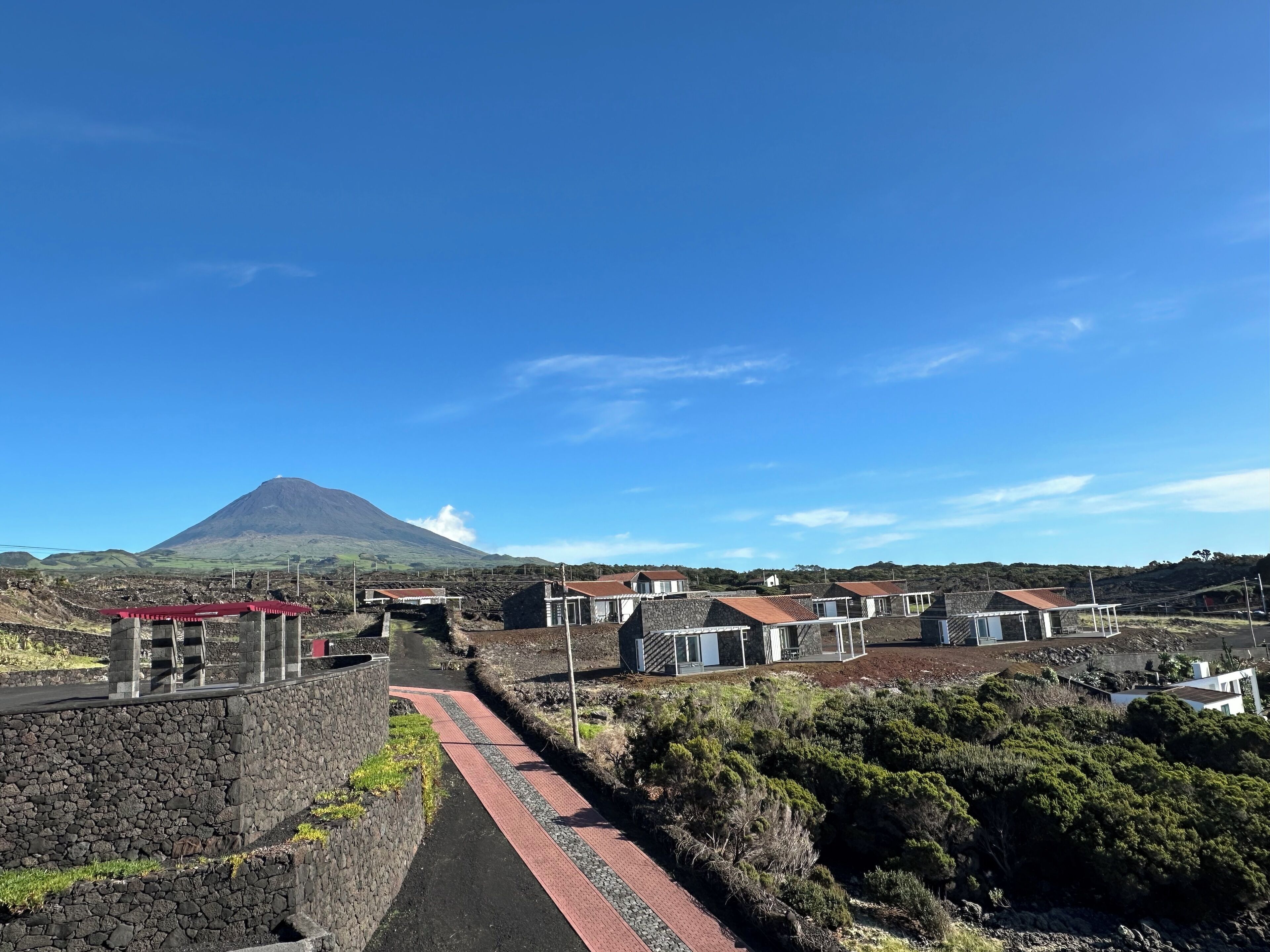 Un pueblo costero con casas de piedra, un sendero pavimentado y una montaña al fondo.