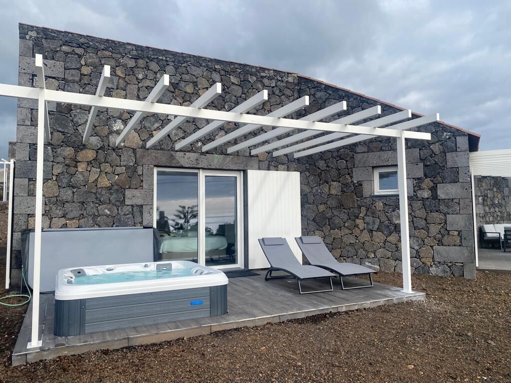 Et moderne udeområde med boblebad, baggrund af stenvæg, pergola og to liggestole.