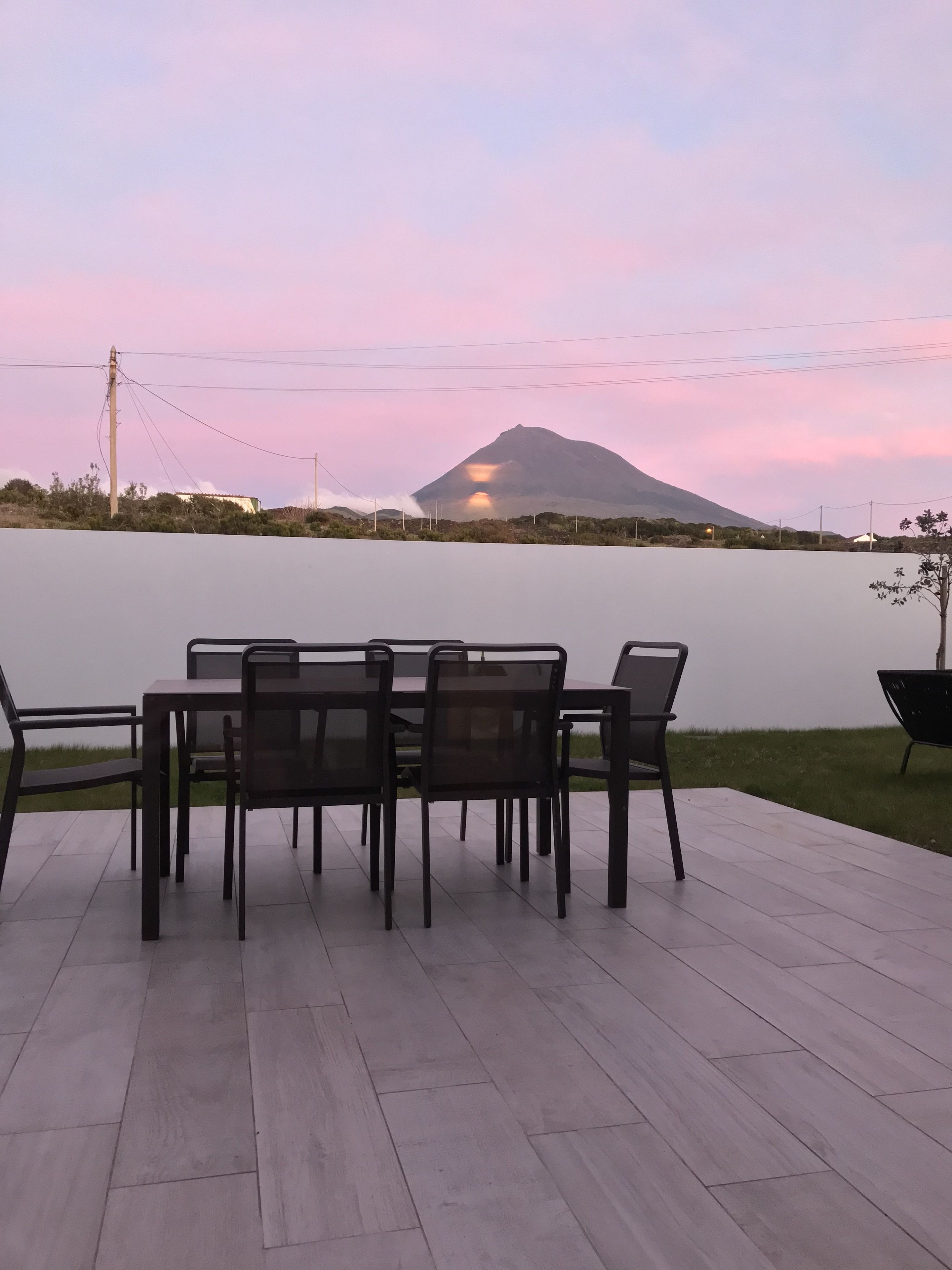 Un patio con mesa y sillas que da a un cuerpo de agua y una montaña.