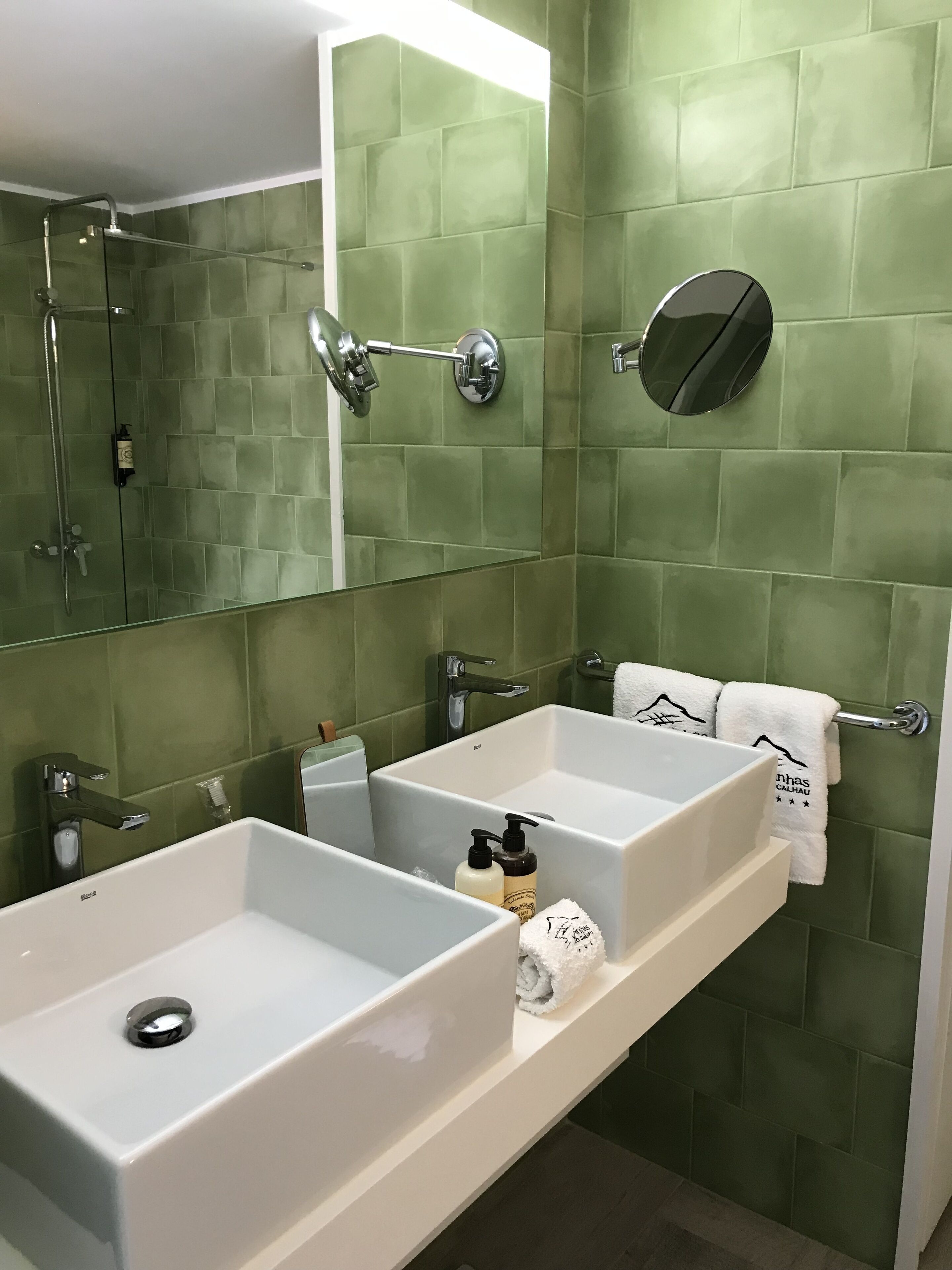 Casa de banho com duas lavatórios, um espelho e chuveiro.