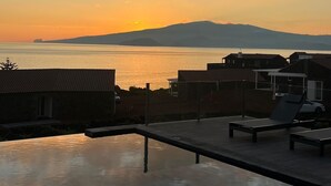 Zona junto a la piscina con sillones de descanso y vista al atardecer sobre el agua.