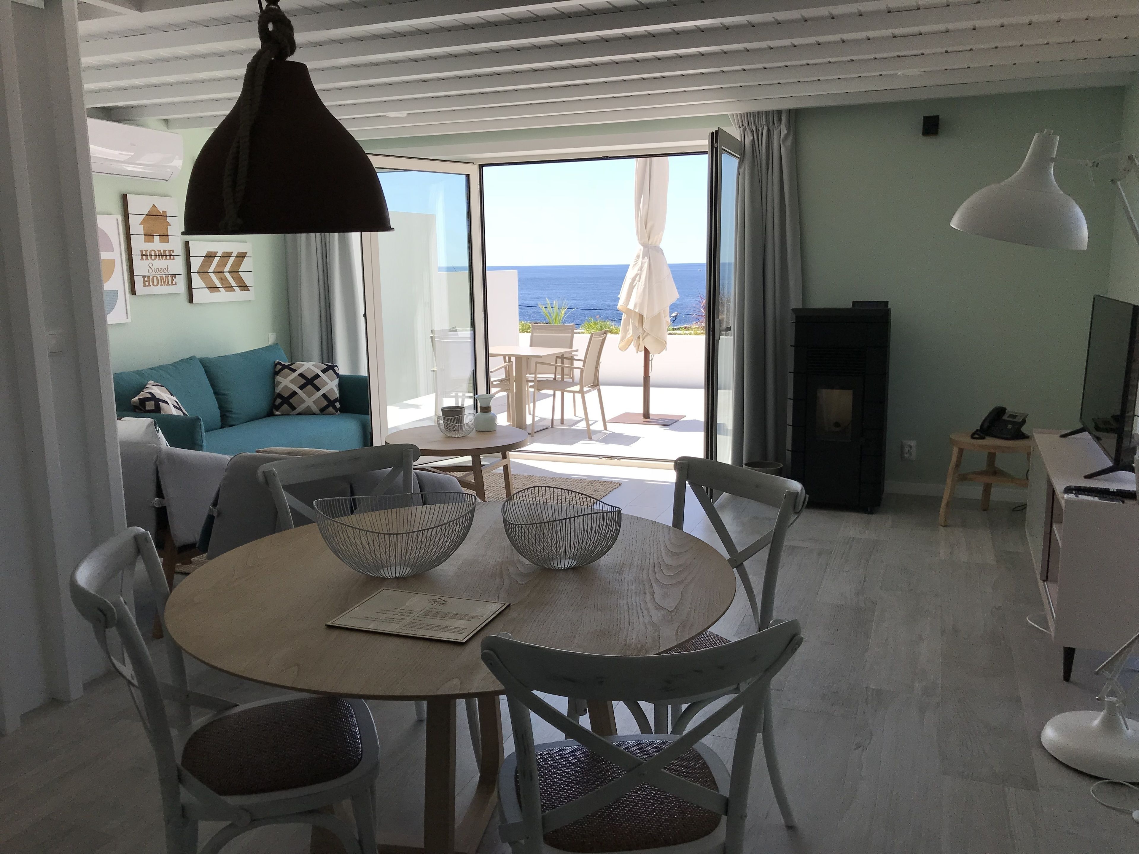 A modern living room with a dining area, large windows, and a view of the sea.