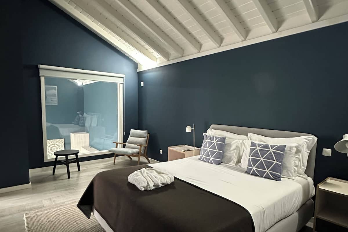 A modern bedroom with a large bed, a window, a chair, and a nightstand.