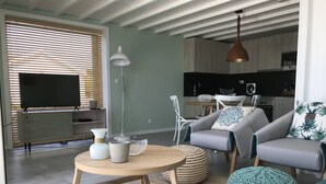 Una sala de estar moderna con sofá, una mesita de centro y elementos decorativos. Se ve una cocina al fondo.