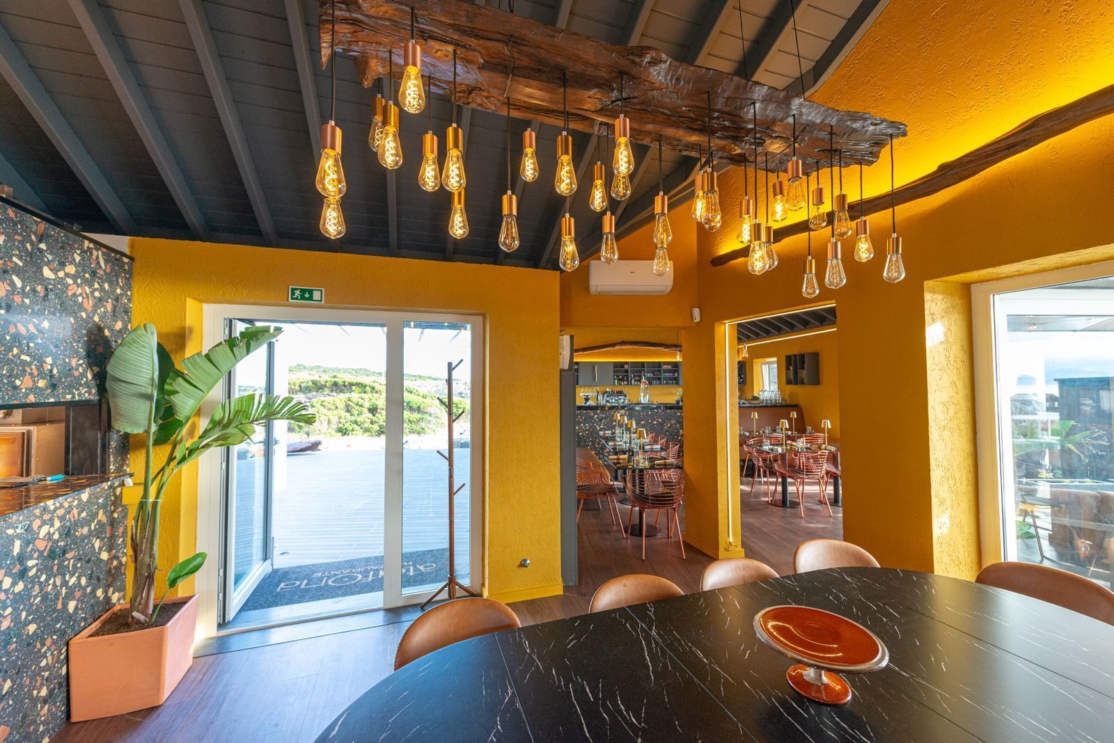 Un restaurant avec une table en marbre noir, des luminaires suspendus et une vue sur l’eau.