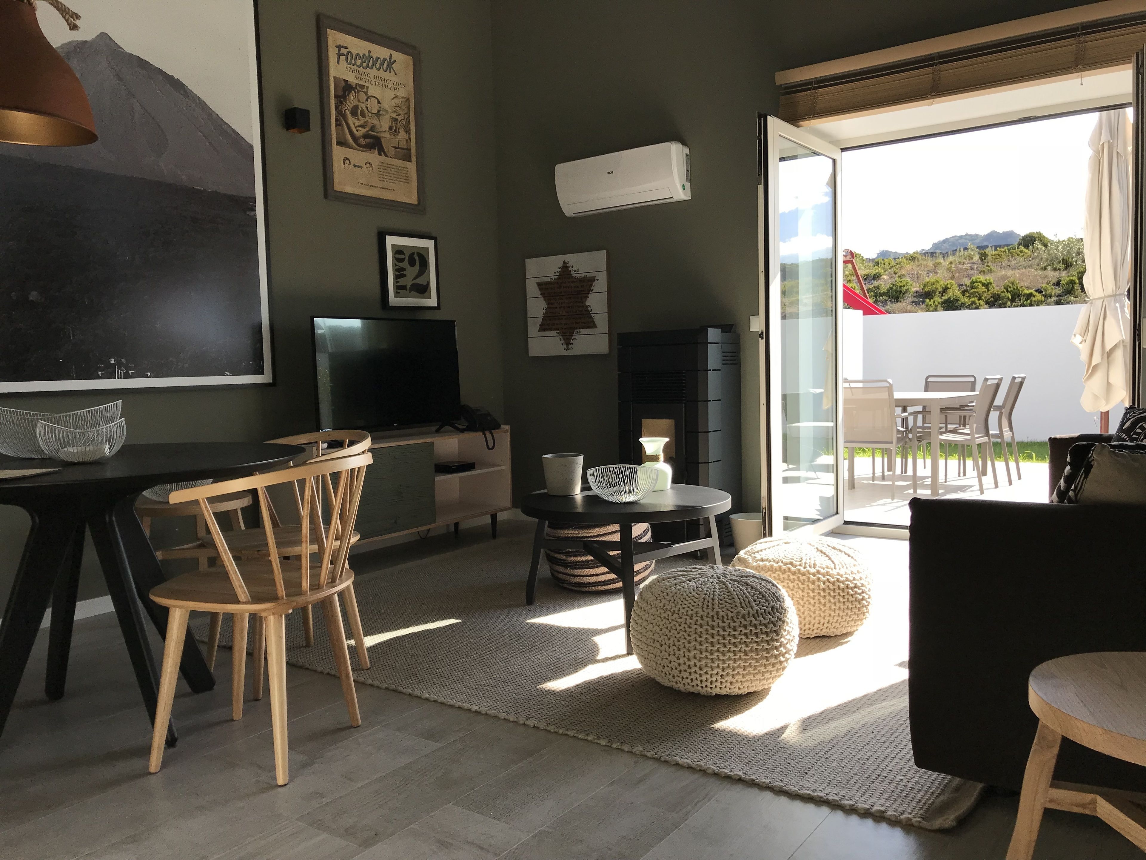 A living room with a flat-screen TV, a fireplace, a dining area with chairs, and a view of the outdoors.