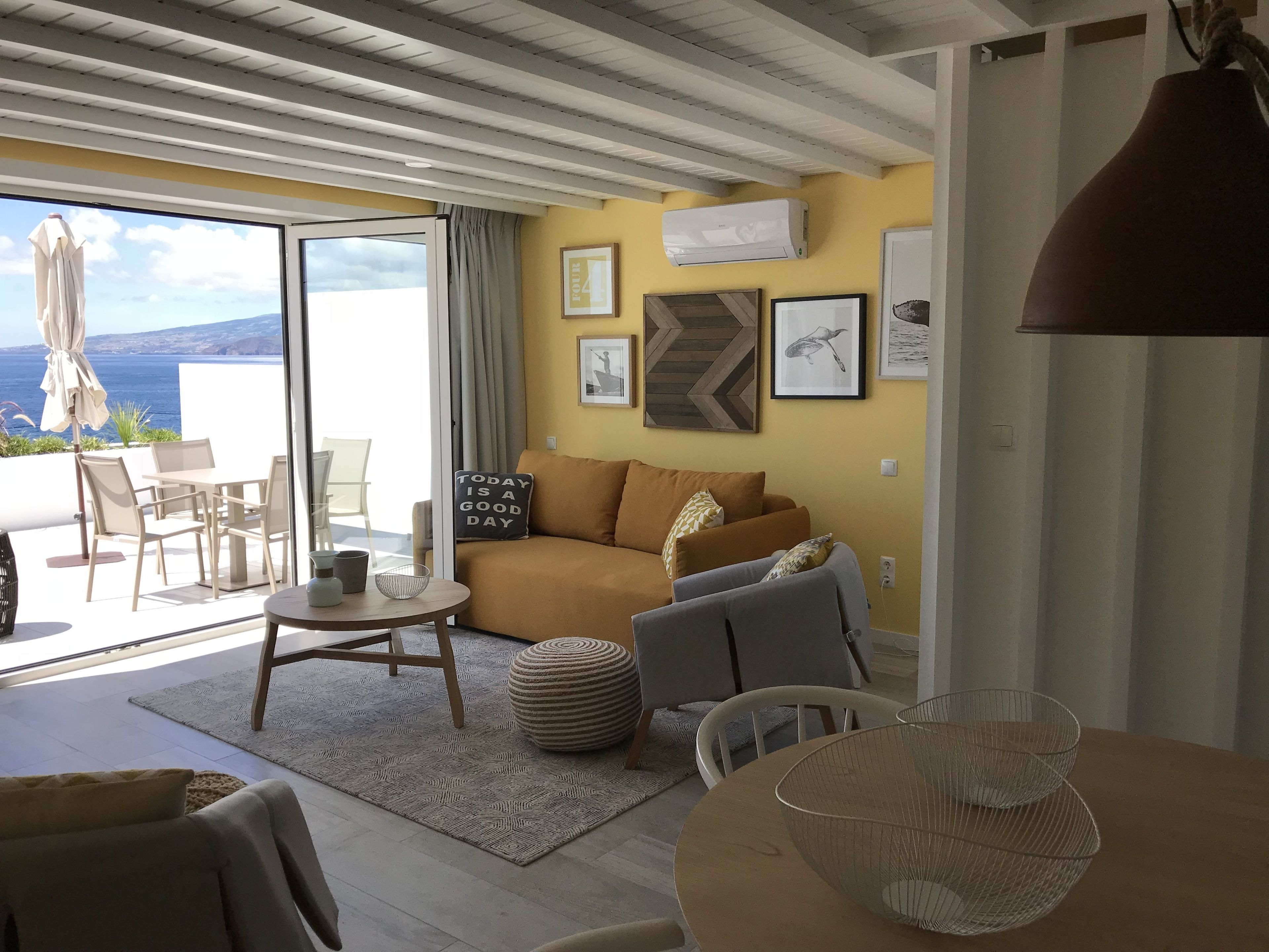 A living room with a sofa, chairs, a table, and a view of the sea.