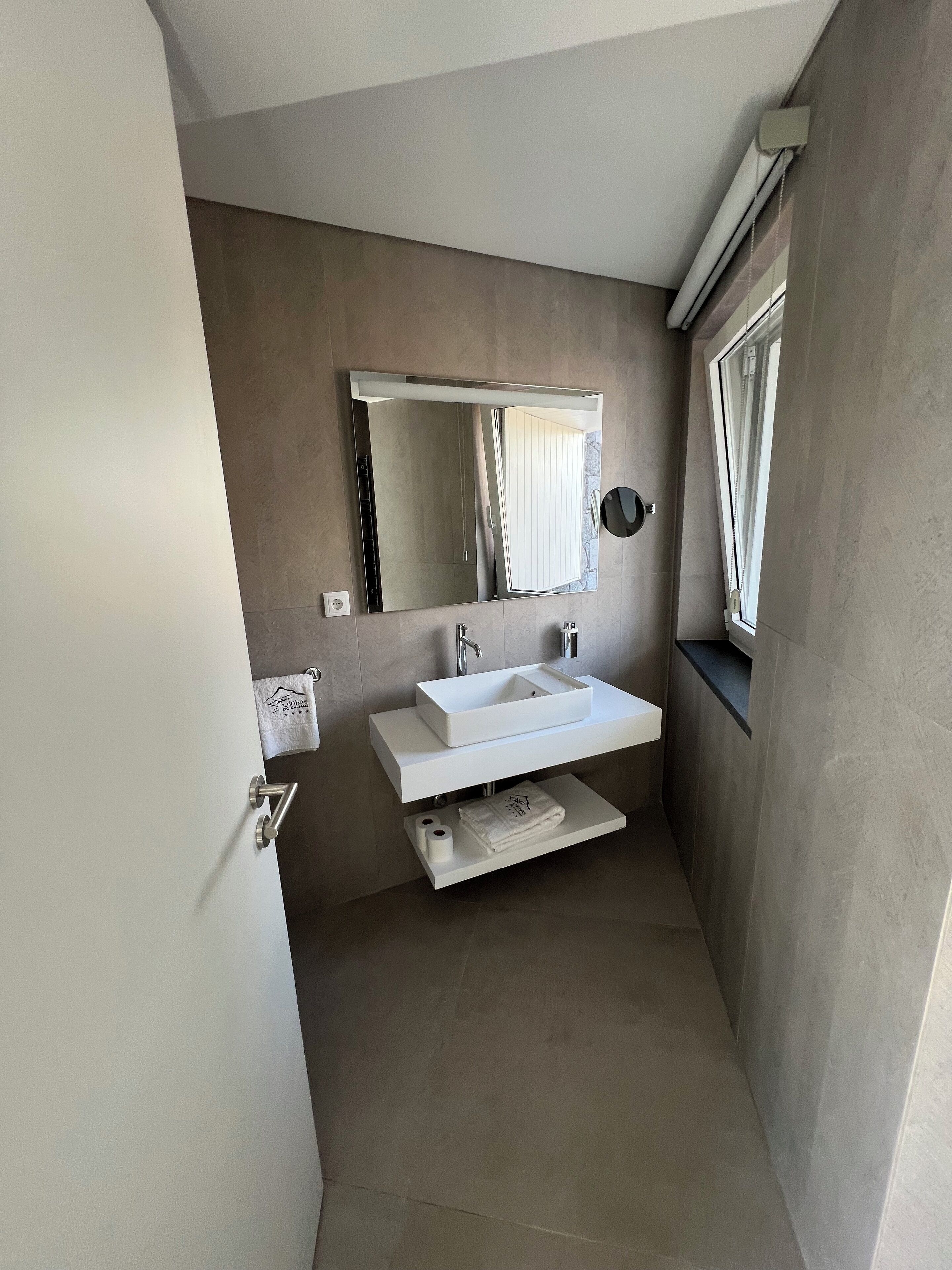 Un baño moderno con un espejo grande, un lavabo blanco y un perchero para toallas.