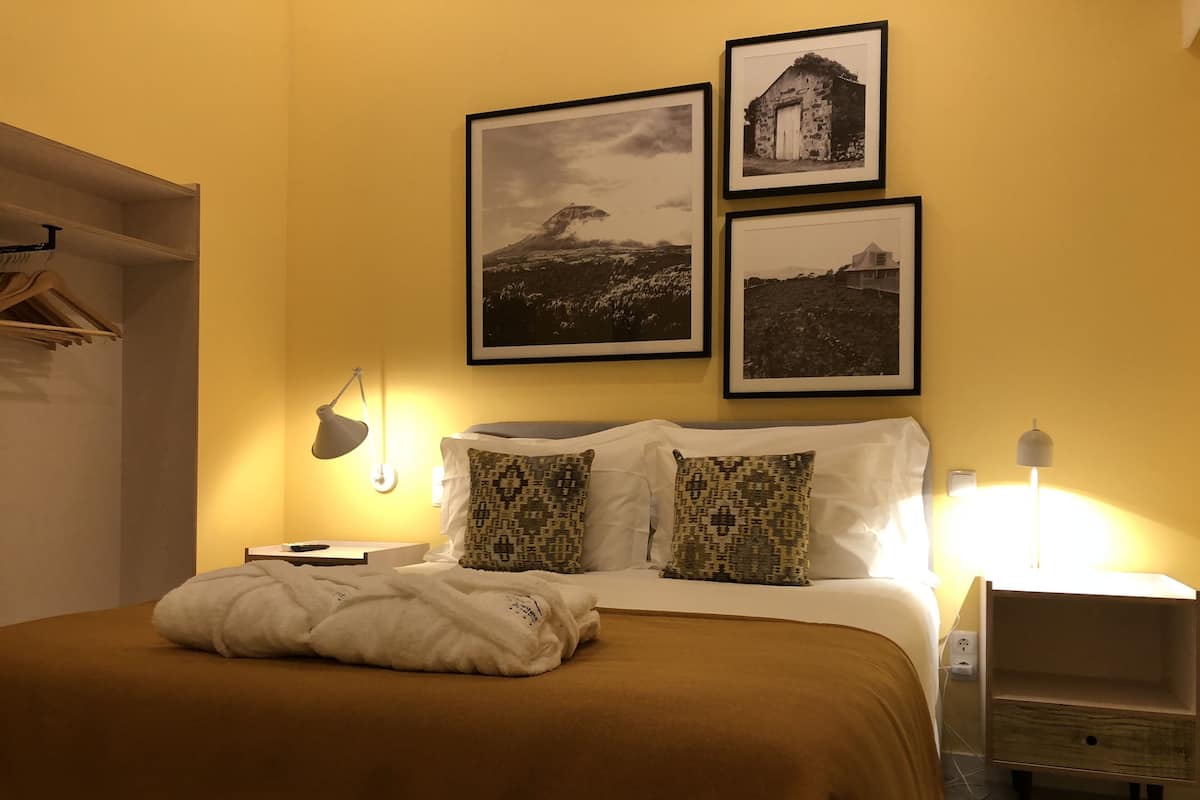 A hotel room with a bed, two pillows, a bedside table, a lamp, and three framed pictures on the wall.