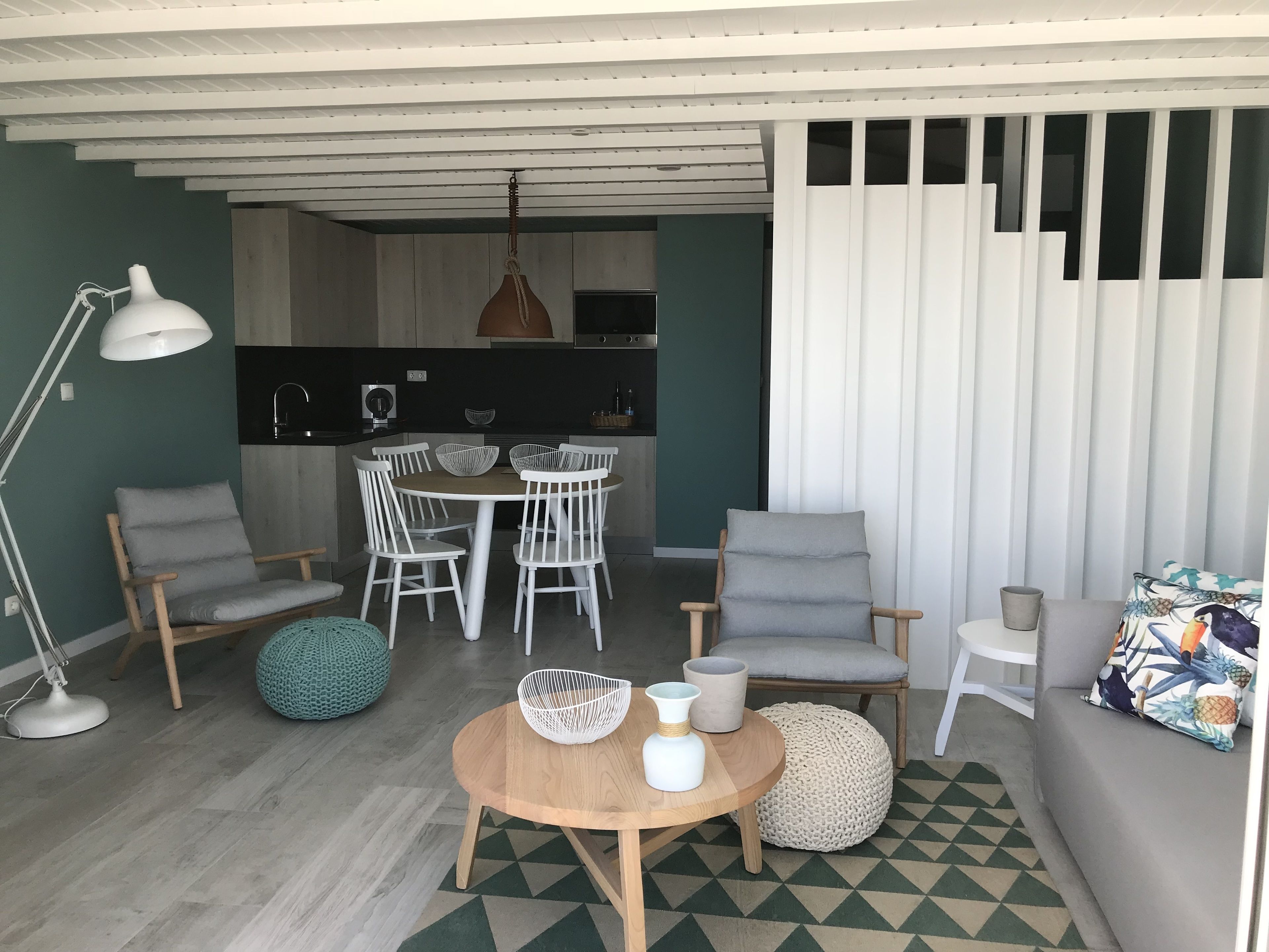 Een moderne woonkamer met een ronde houten salontafel, witte stoelen, een grijze bank en een vloerkleed met een patroon.