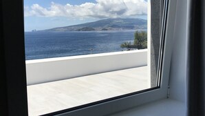 Una ventana con vista al mar y una cadena montañosa distante.