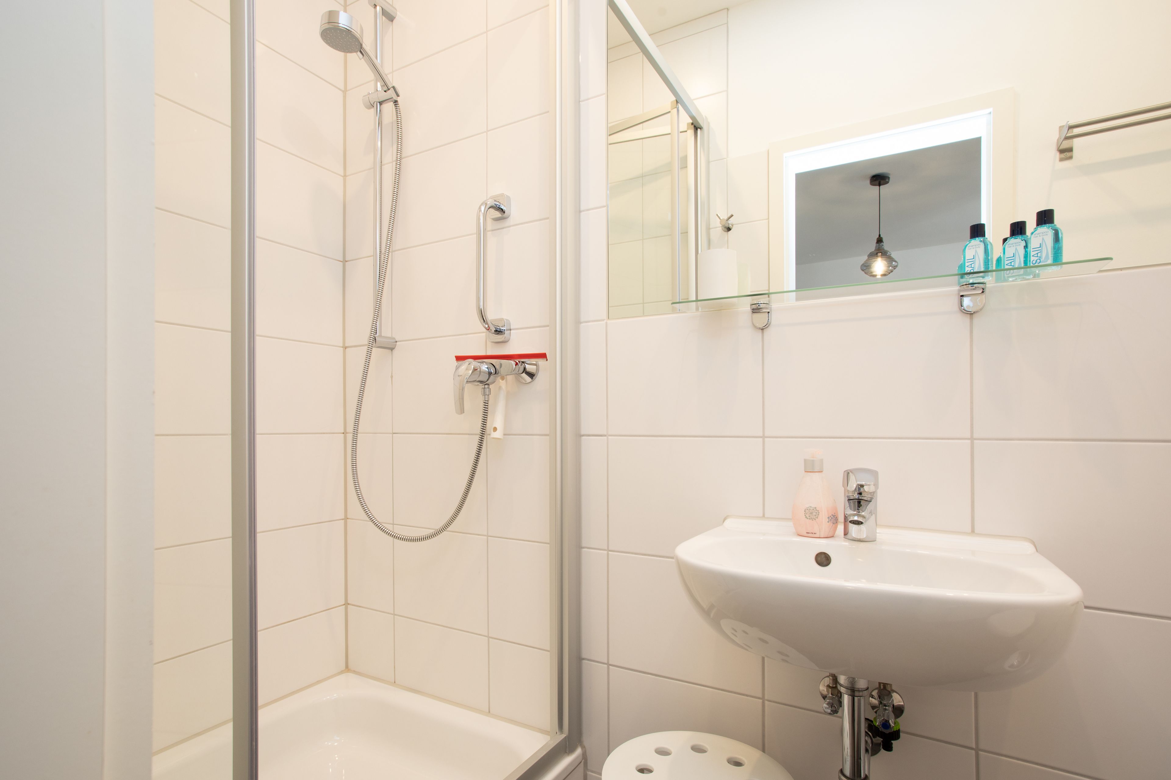 Ein modernes Badezimmer mit einer Duschkabine aus Glas, einem weißen Waschbecken und einem Spiegel darüber.