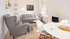 A modern living room with a grey sofa, a grey armchair, a white dining table, and a TV. - Wertschätzer II - Unter der Wehme (Detmold)