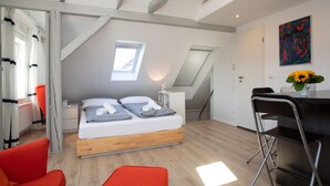 A modern bedroom with a loft bed, a skylight, a desk with a chair, and a colorful abstract painting. - Wertschätzer II - Unter der Wehme (Detmold)
