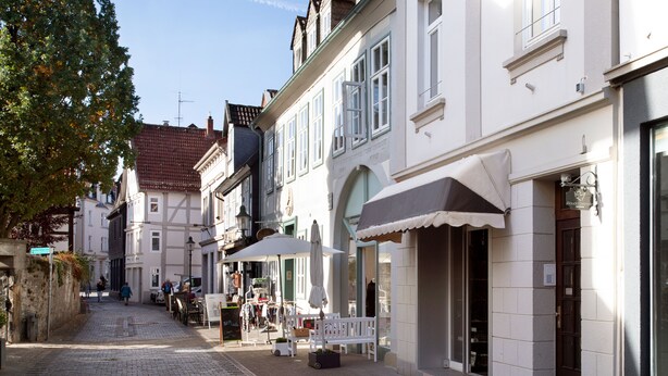 A cobblestone street lined with traditional European buildings, some with outdoor seating and umbrellas. - Wertschätzer II - Unter der Wehme (Detmold)
