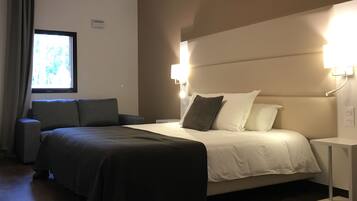 A hotel room with a bed, bedside tables, a window with curtains, and a wall-mounted light fixture.