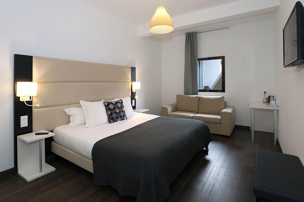 A modern hotel room with a large bed, a sofa, a small table, and a TV.