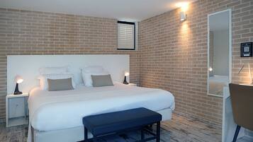 Un dormitorio moderno con una cama grande, lámparas de noche, un banco, un espejo y una pared de ladrillo.
