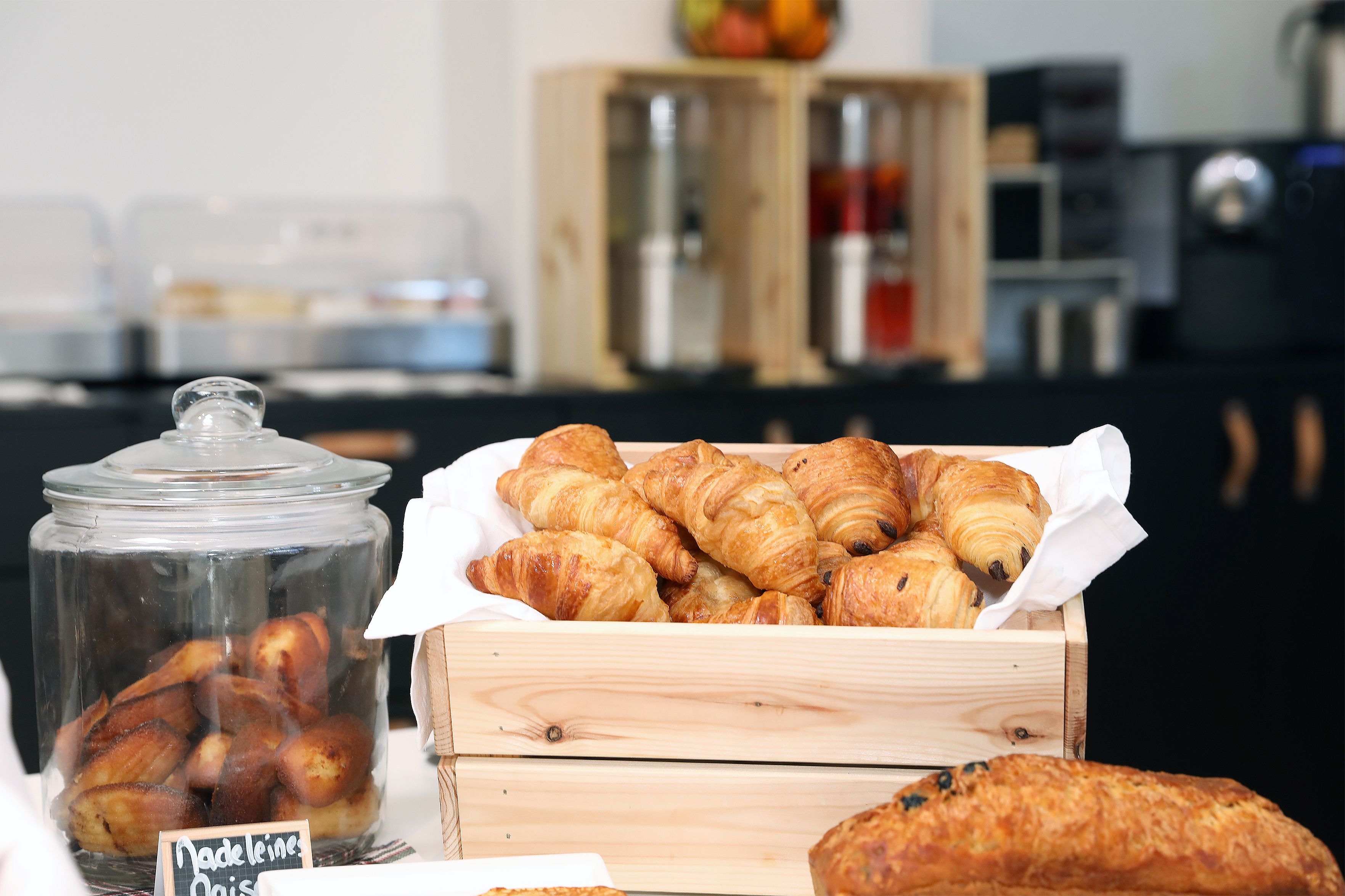 A display of assorted pastries in a wooden box and a glass jar, with a sign indicating 'Nadeleine Oiselle'.
