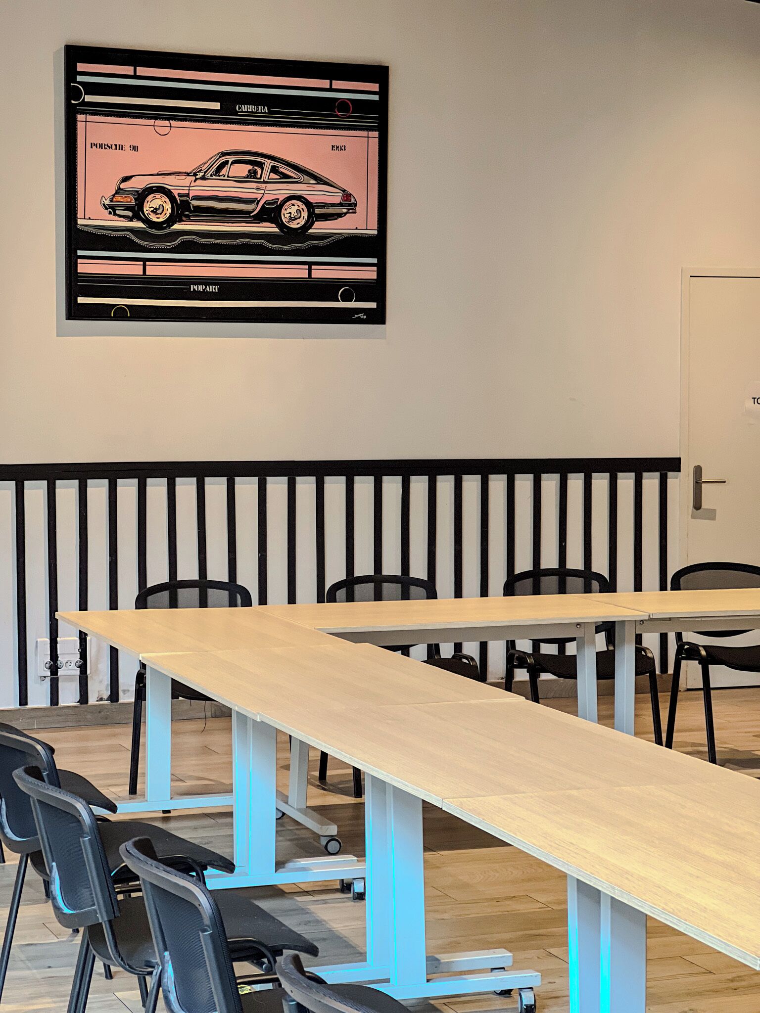 A conference room with a long table, chairs, and a framed car illustration on the wall.