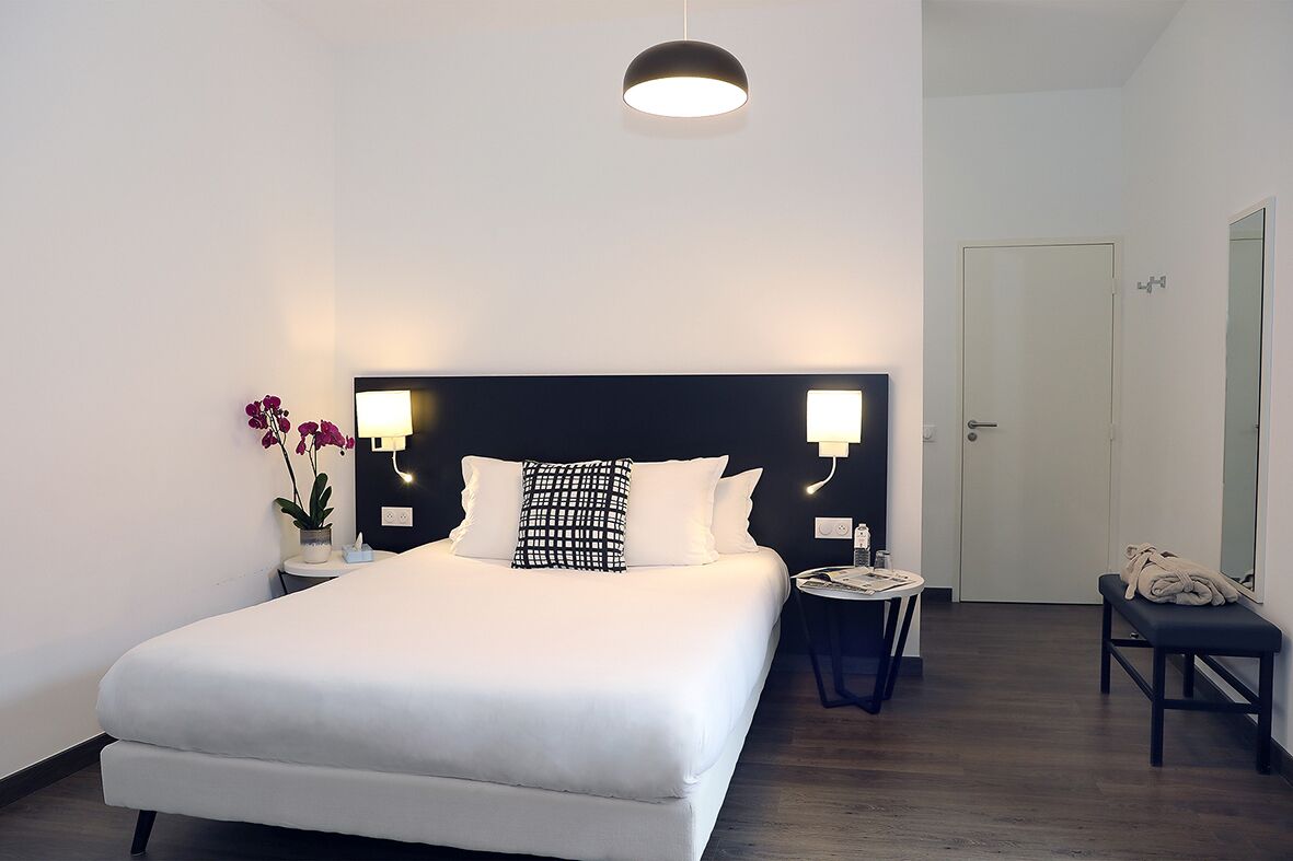 Une chambre d’hôtel bien aménagée, avec un grand lit, des lampes de chevet, une petite table et un banc.