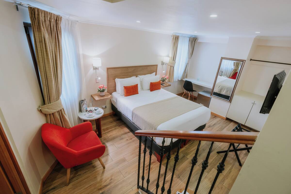 Ein Hotelzimmer mit einem Bett, einem roten Sessel, einem kleinen Tisch mit einer Lampe und einem Spiegel an der Wand.