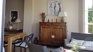 Una sala de estar acogedora con una mesa de comedor de madera, muebles de mimbre, un aparador con adornos y un cuadro en la pared.
