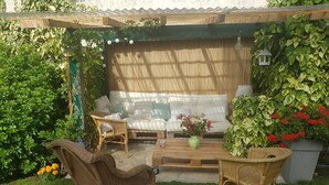 Un espacio exterior acogedor con un sofá, dos sillones de mimbre, una mesita de centro y una planta en maceta.