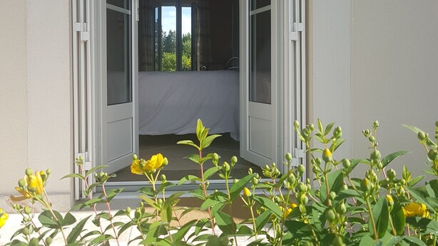 Una puerta abierta que da a una habitación con cama, candelabro y vistas a árboles.