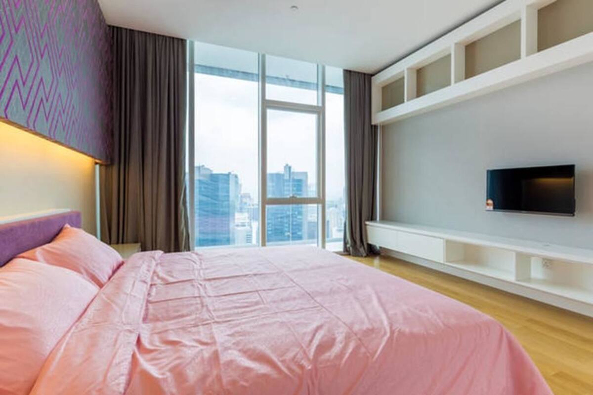 Une chambre d’hôtel moderne dotée d’un grand lit, d’un téléviseur fixé au mur et offrant une vue sur la ville grâce à de grandes fenêtres.