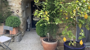 A stone archway leading to a courtyard with potted plants, a small table, and a chair. - Maison d'hôtes La Cour des Lauriers (Saint-Hippolyte-de-Montaigu)