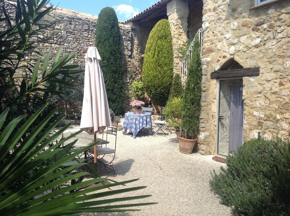 A stone building with a gravel patio, a table with a blue tablecloth, and potted plants. - Maison d'hôtes La Cour des Lauriers (Saint-Hippolyte-de-Montaigu)