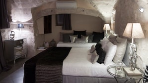 A bedroom with a stone arch ceiling, a bed with white bedding, a bedside table with a lamp, and a small table with a glass. - Maison d'hôtes La Cour des Lauriers (Saint-Hippolyte-de-Montaigu)