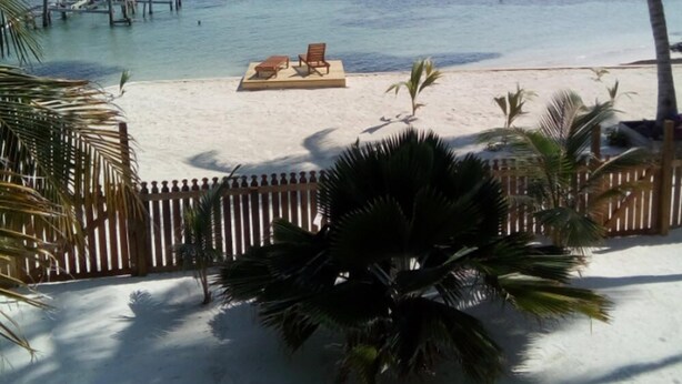 A beach with a wooden pier extending into the water, a sandy area with a small table and chairs, and palm trees. - Carolyns Other House (Caye Caulker)