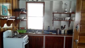 A compact kitchen with wooden cabinets, a stove, and a window providing natural light. - Carolyns Other House (Caye Caulker)