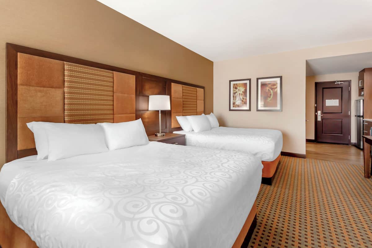 A hotel room with two beds, a nightstand, a lamp, and framed artwork on the wall.