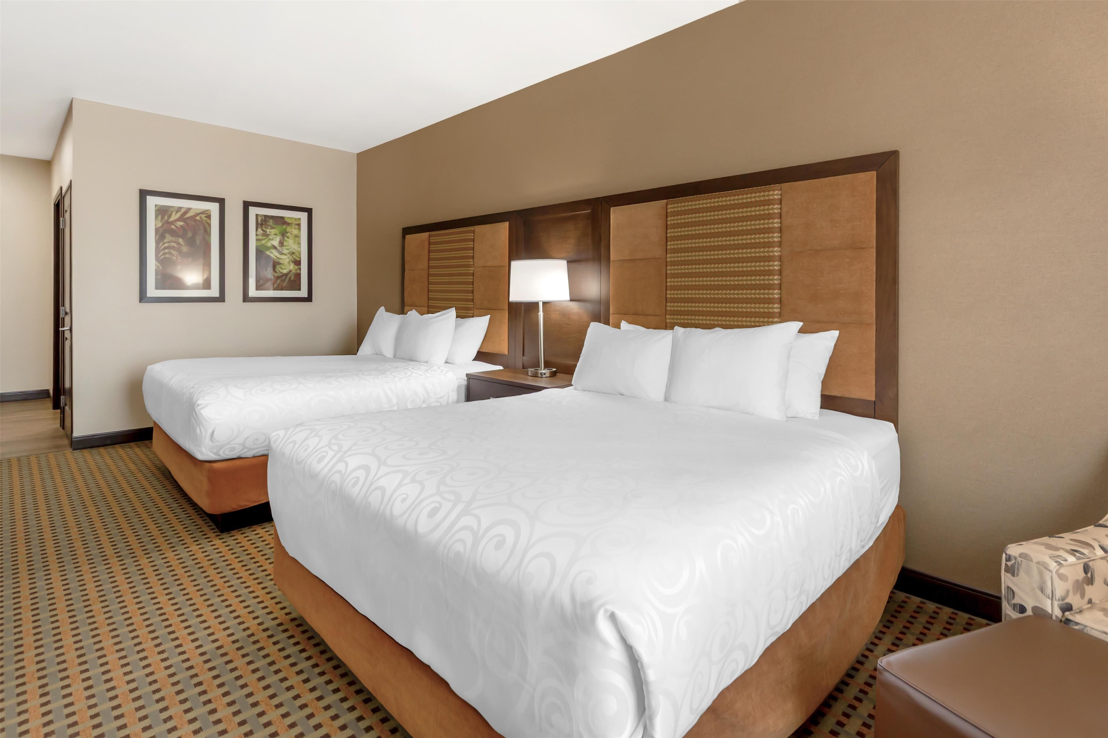 A hotel room with two beds, a nightstand with a lamp, and a patterned carpet.