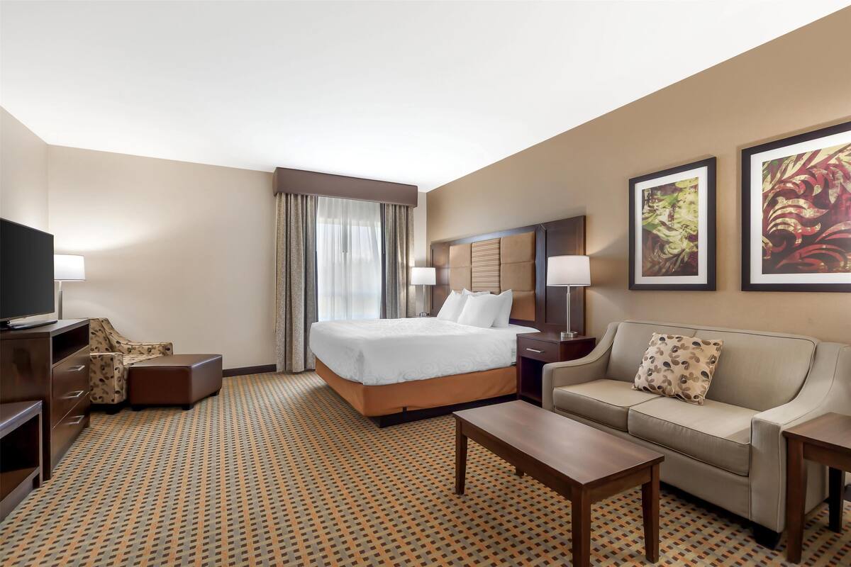 A hotel room with a large bed, a sofa, a coffee table, a TV, and artwork on the walls.