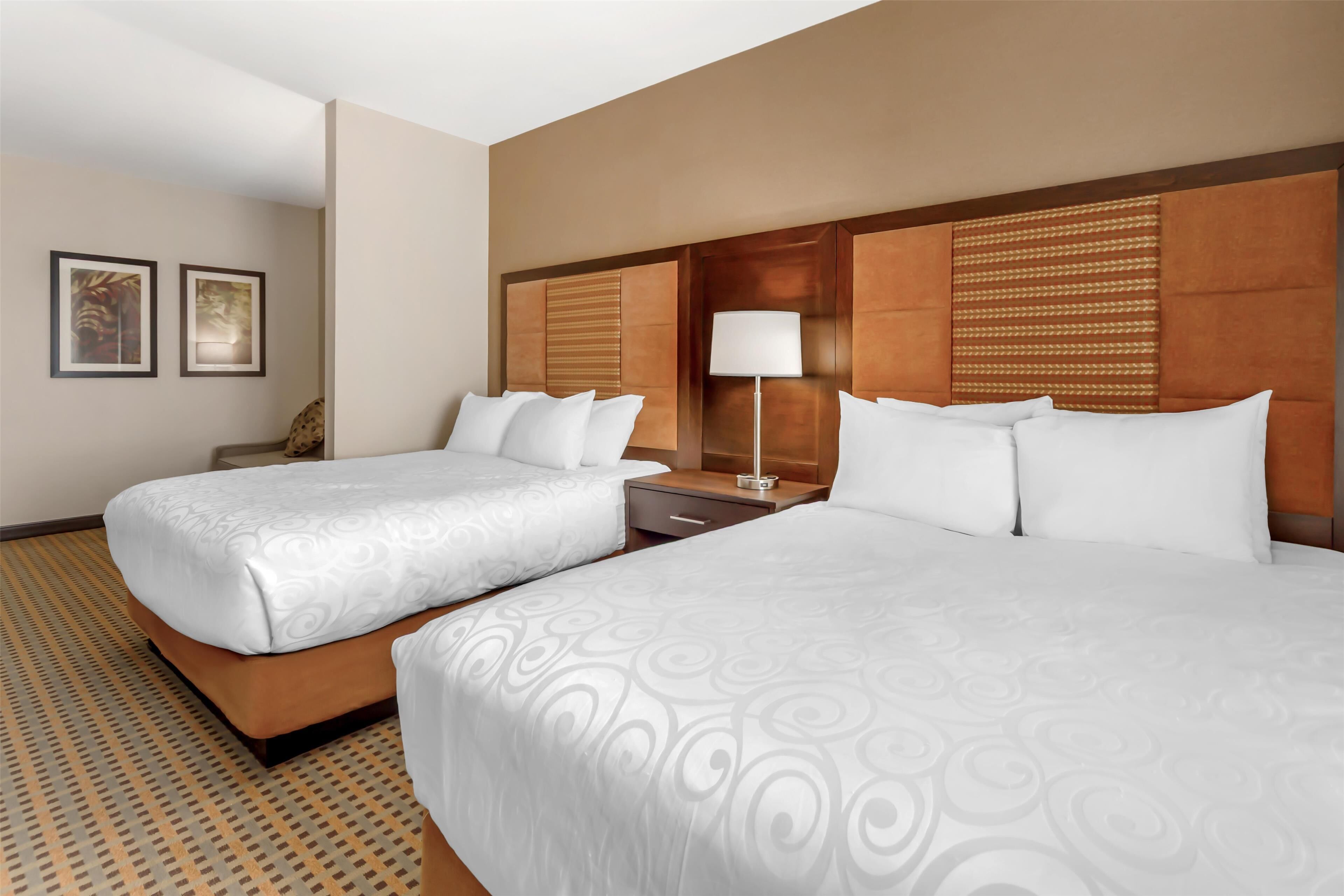 A hotel room with two beds, a nightstand, a lamp, and framed artwork on the wall.