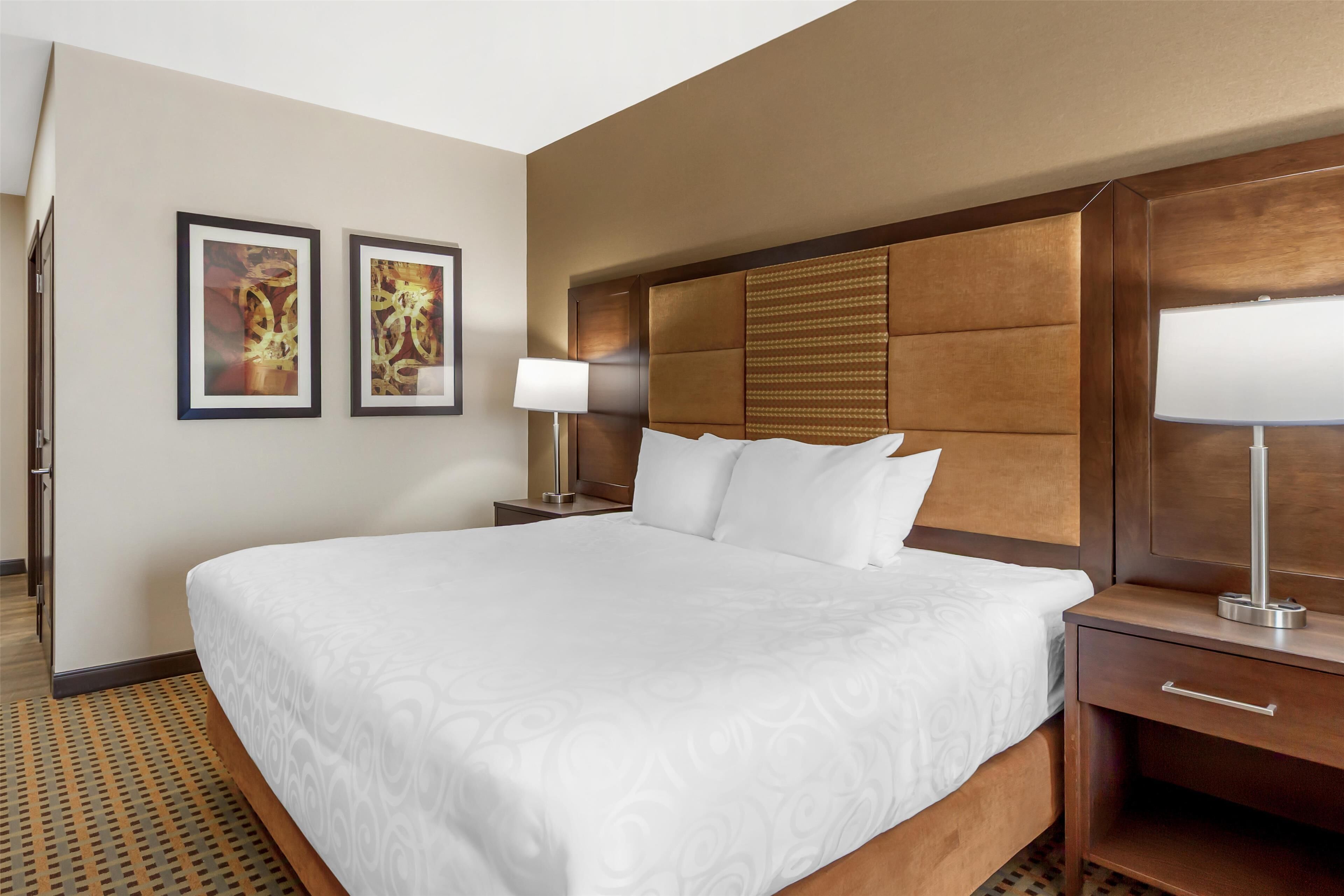A hotel room with a large bed, a wooden headboard, two bedside tables with lamps, and two framed pictures on the wall.