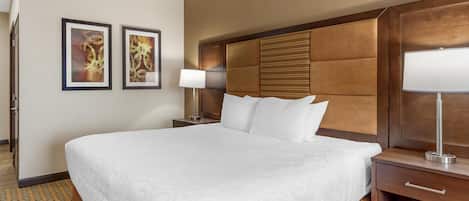 A hotel room with a large bed, a wooden headboard, two bedside tables with lamps, and two framed pictures on the wall.