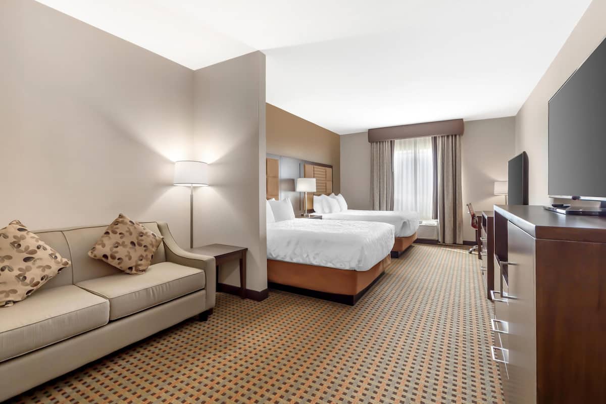 A hotel room with a sofa, two beds, a desk, a TV, and a patterned carpet.