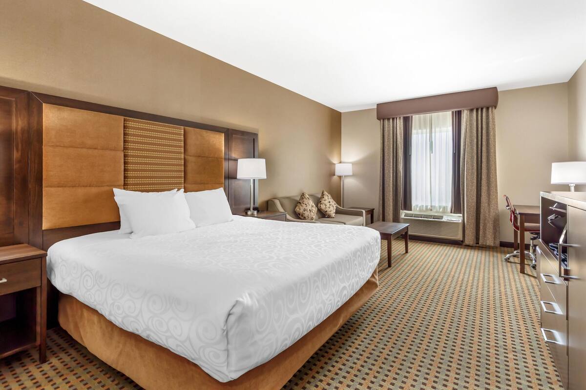 A hotel room with a large bed, a desk, a chair, and a window with curtains.