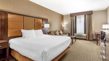 Una habitación de hotel con una cama grande, un escritorio, una silla y un ventanal con cortinas.