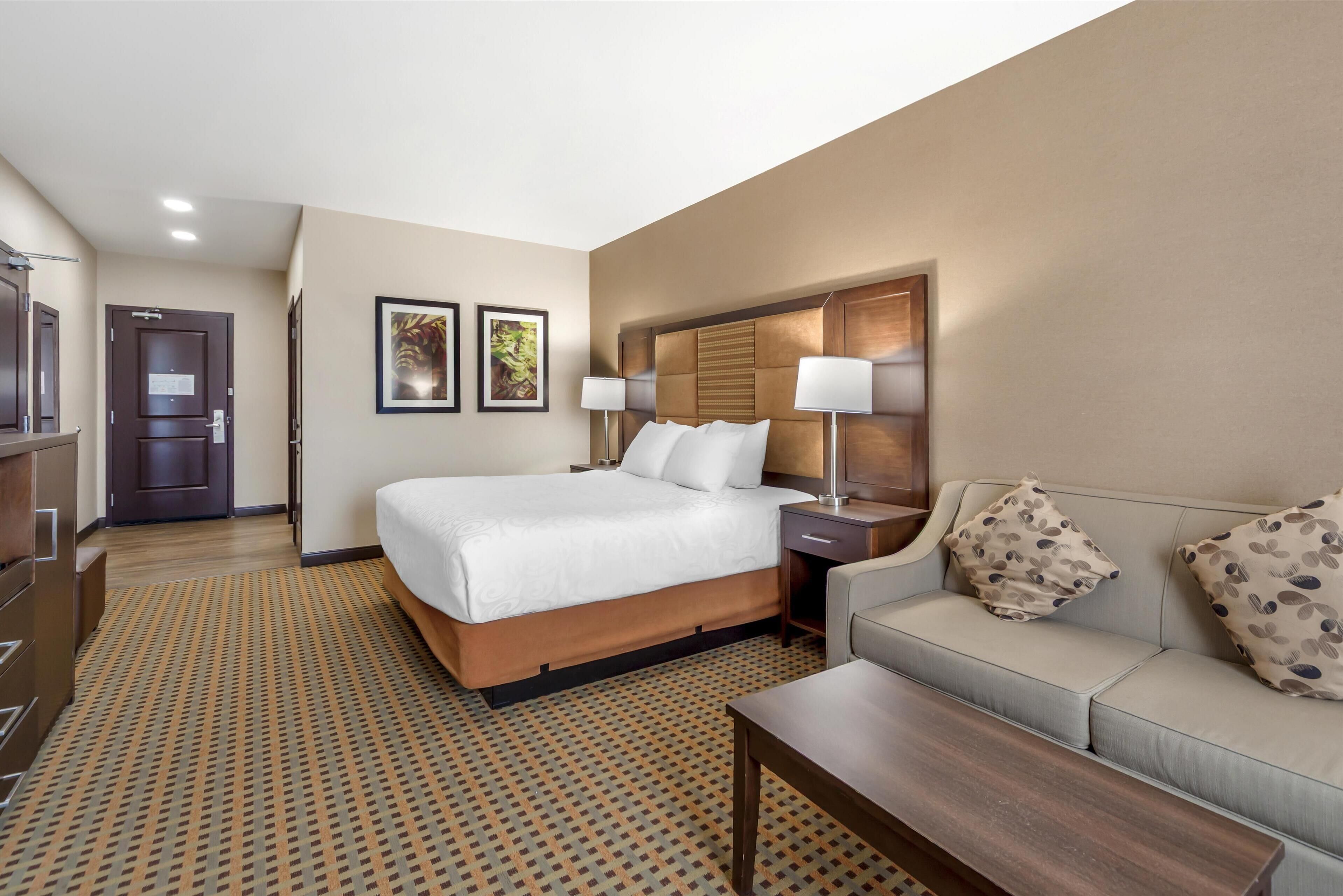 A hotel room with a large bed, a sofa, a coffee table, and a desk with a lamp.