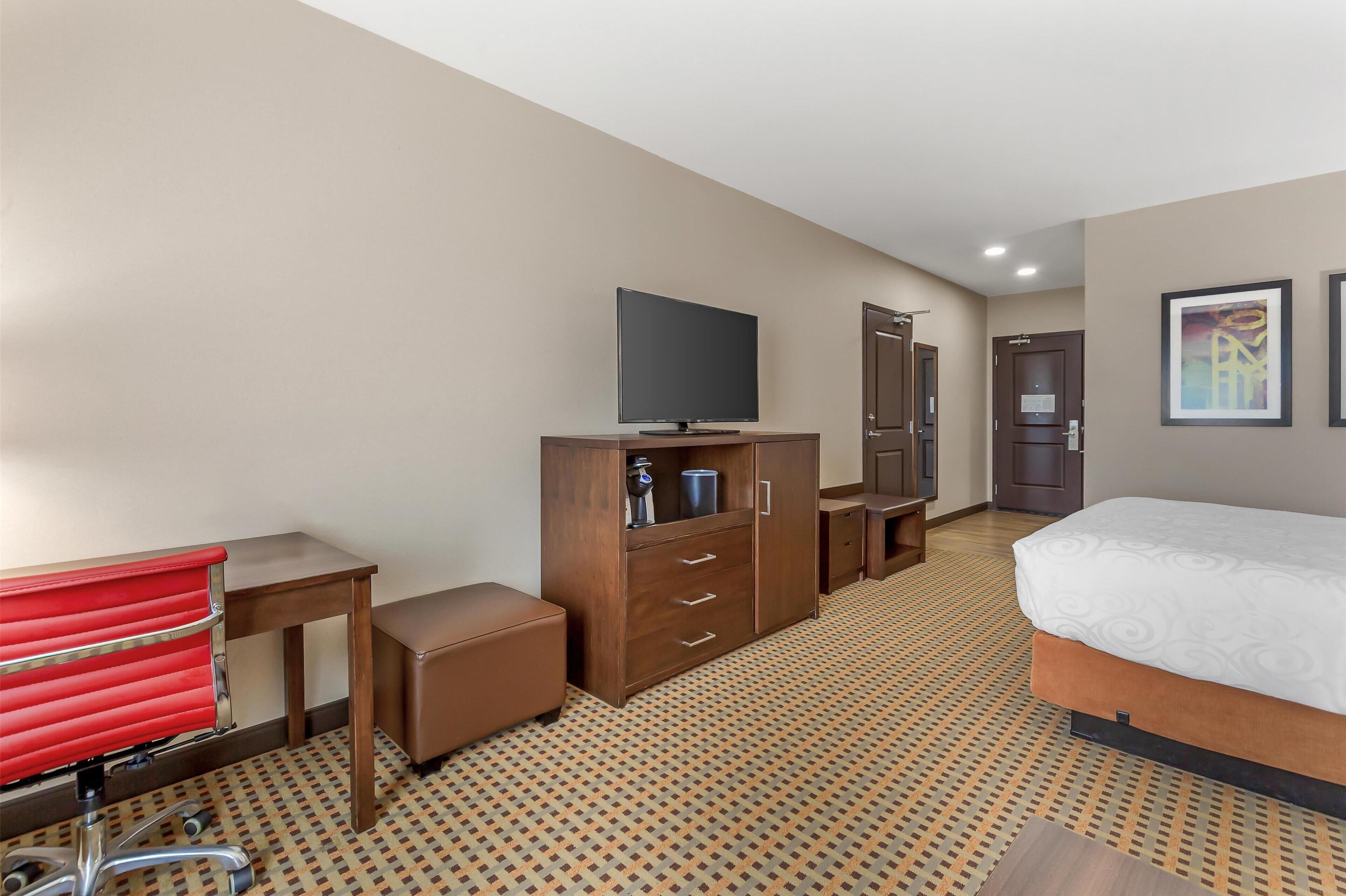 Ein Hotelzimmer mit Bett, Fernseher, Holzschrank, Schreibtisch und einem roten Sessel.