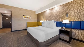 Une chambre d’hôtel avec un lit, des tables de chevet, une horloge murale et une porte.