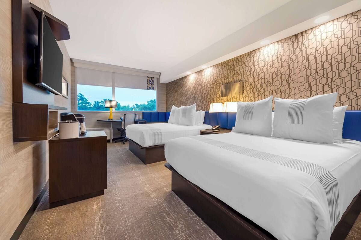 Una habitación de hotel con dos camas, un escritorio, un televisor y un ventanal grande.