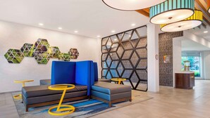 Un moderno vestíbulo con un sofá modular, mesas amarillas y arte geométrico en la pared.