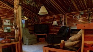A rustic cabin interior with wooden walls, a television, a sofa, and a dining table. - Cedar Cabin Located on a Buffalo Farm Near the Buffalo National River (Marshall)
